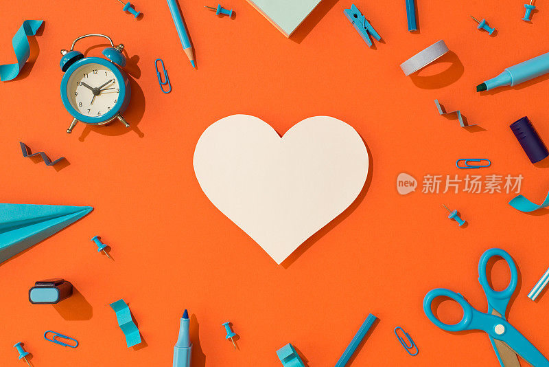 Top view photo of white paper heart and blue school supplies stationery alarm clock markers铅笔剪刀paper airplane adhesive tape clips and pins on isolated orange background with blank space白色纸心形和蓝色学校用品的俯视图照片